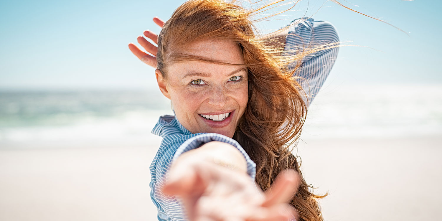 Ältere Frau mit roten Haaren und Sommersprossen am Strand lächelnd 